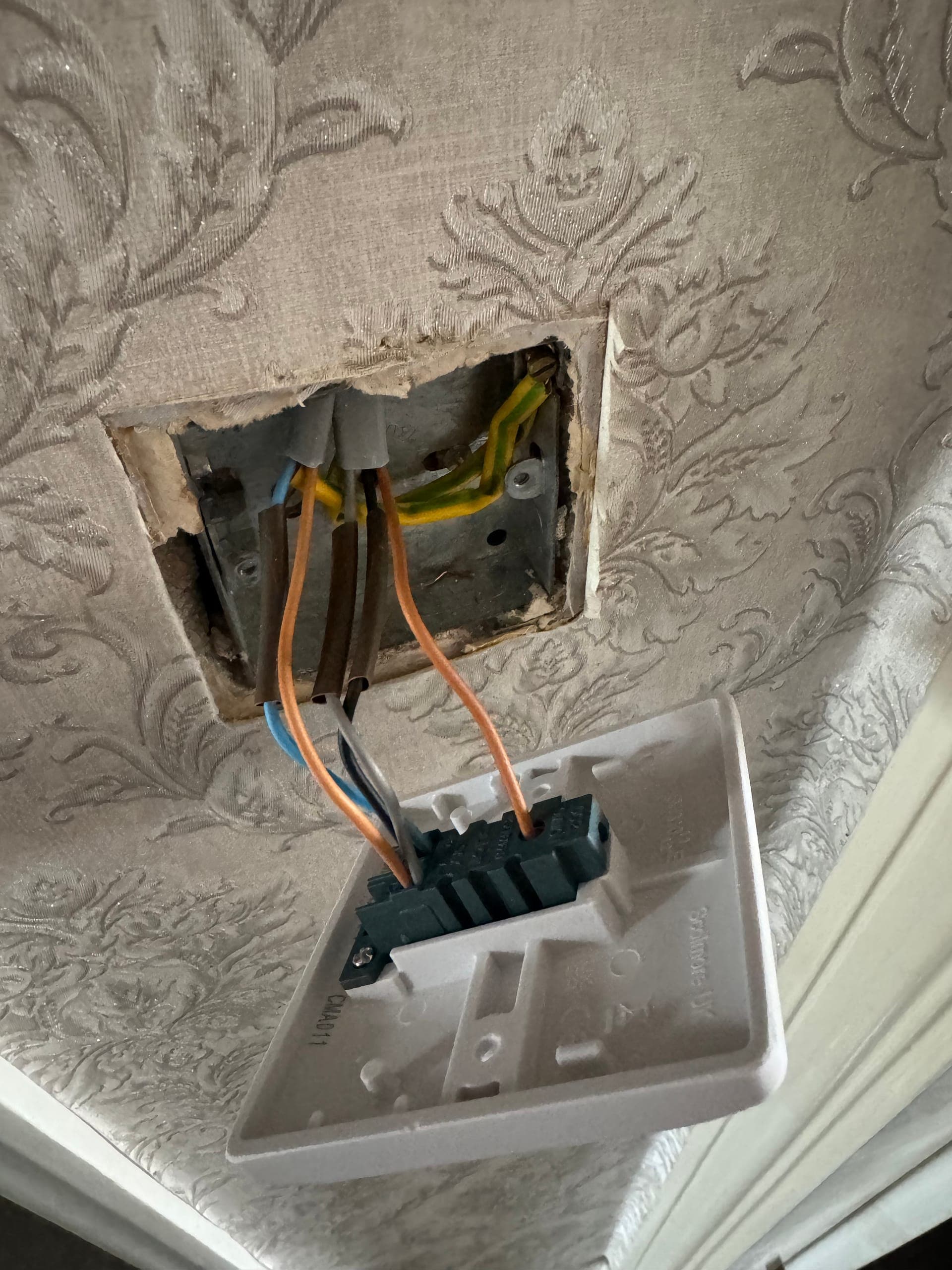 Light switch drawn out of a metal back box in a wallpapered wall, showing sleeved earths and switch wiring