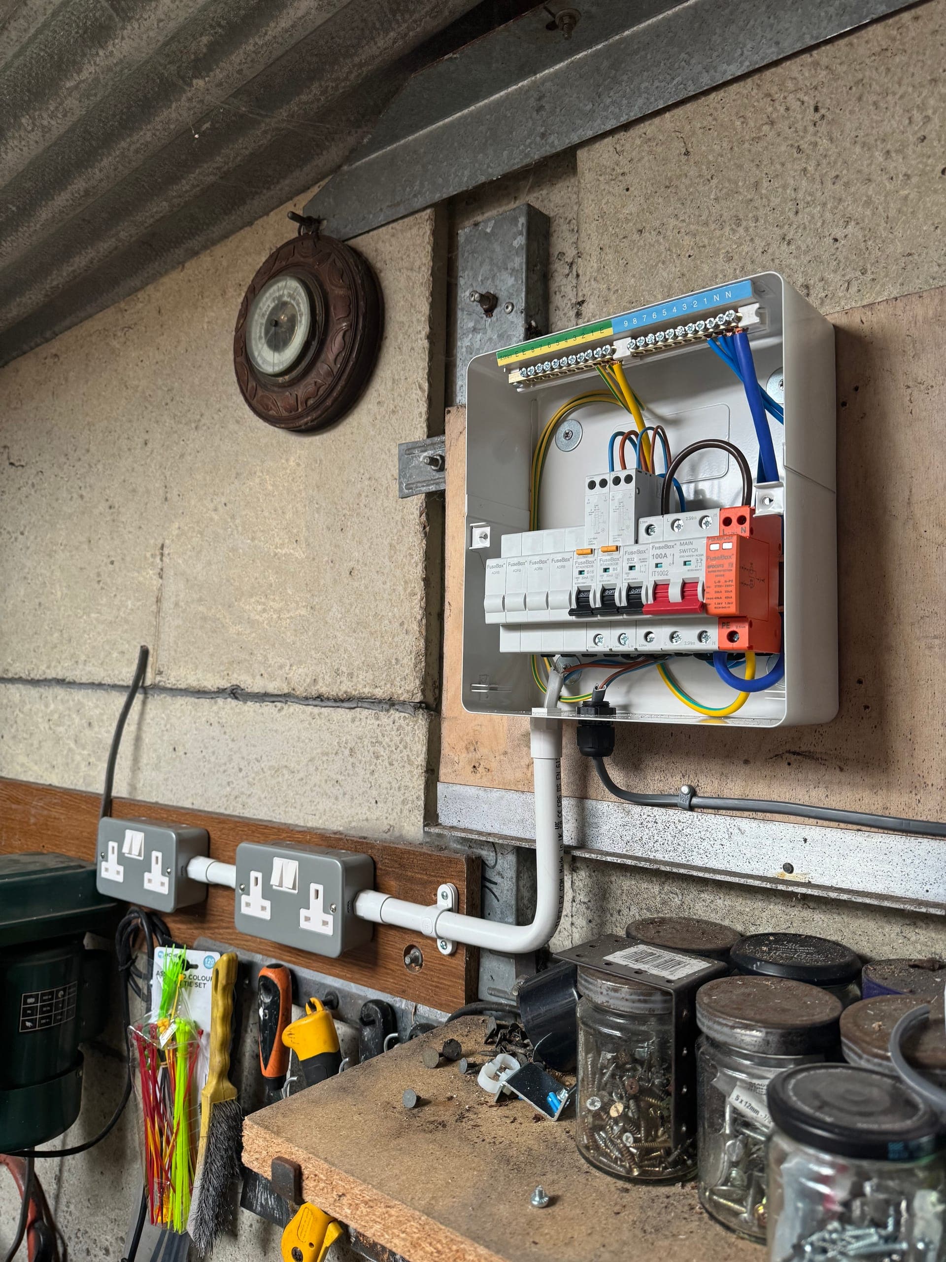 Garage consumer unit with surge protection feeding surface-mounted sockets along a timber batten above a workbench