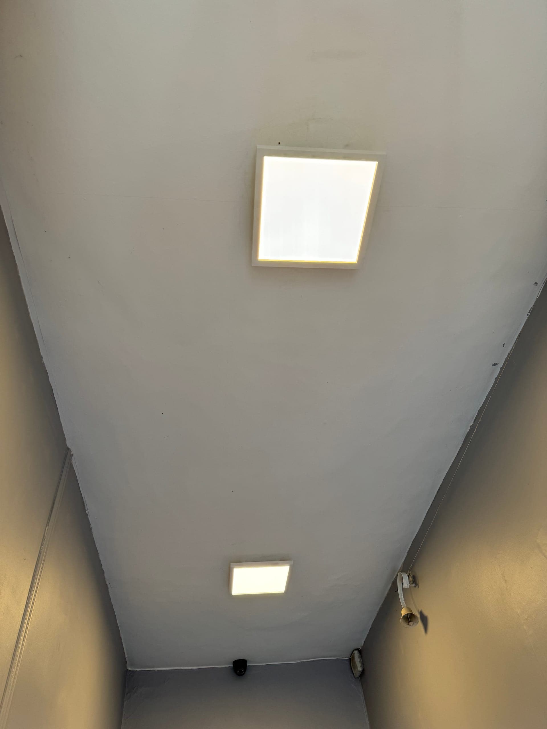 Two square LED panels lighting a stairwell ceiling