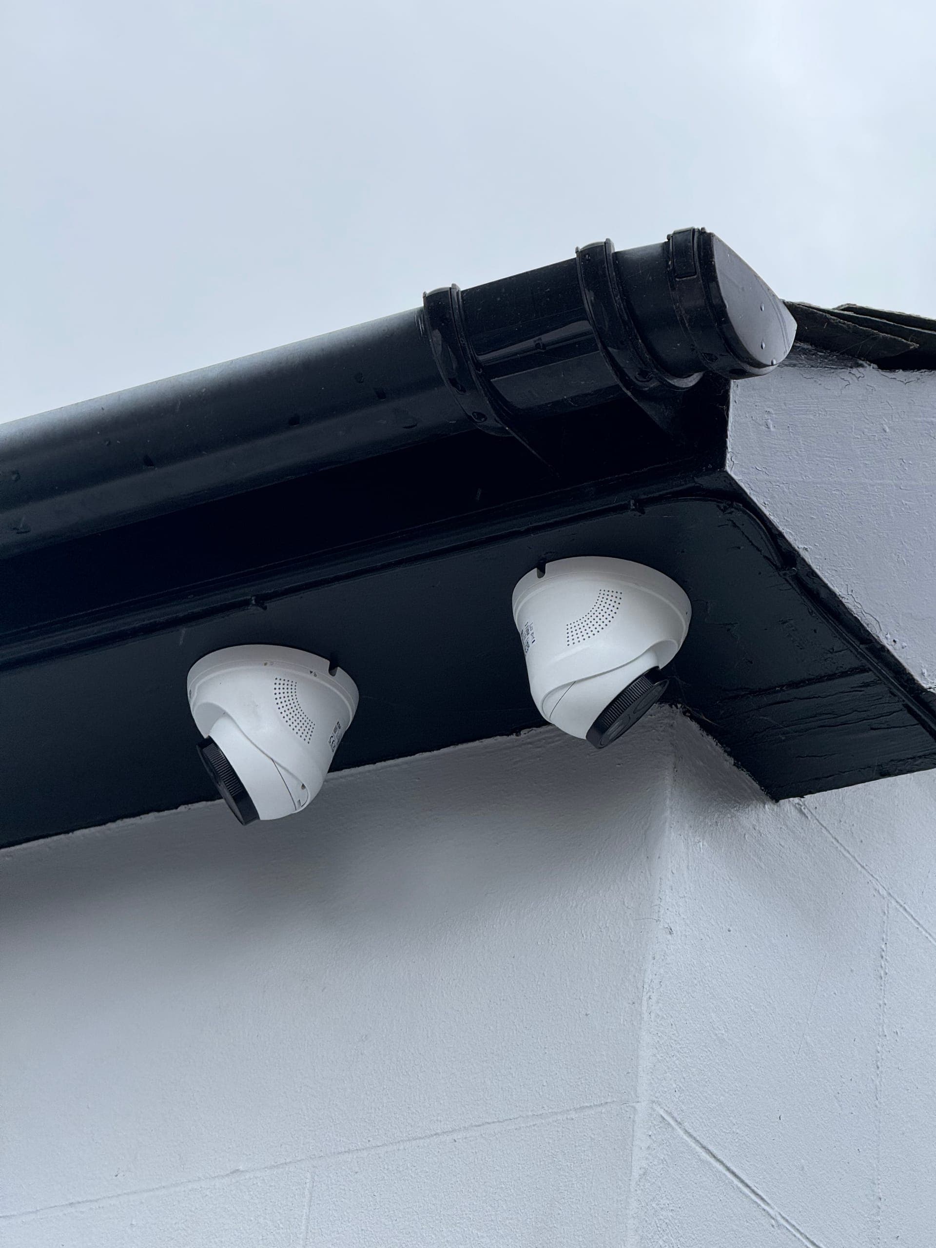 Pair of dome CCTV cameras mounted under the eaves of a rendered house