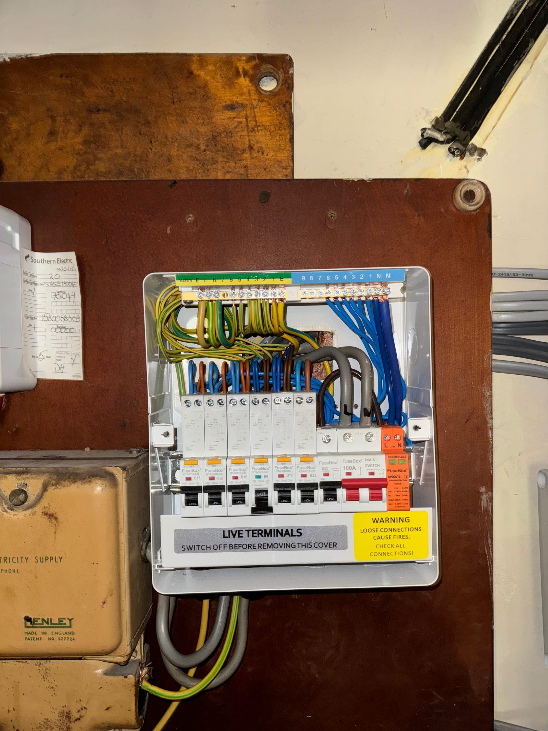 Replacement consumer unit with RCBOs and surge protection on a workshop backboard, beside the original Henley block and meter