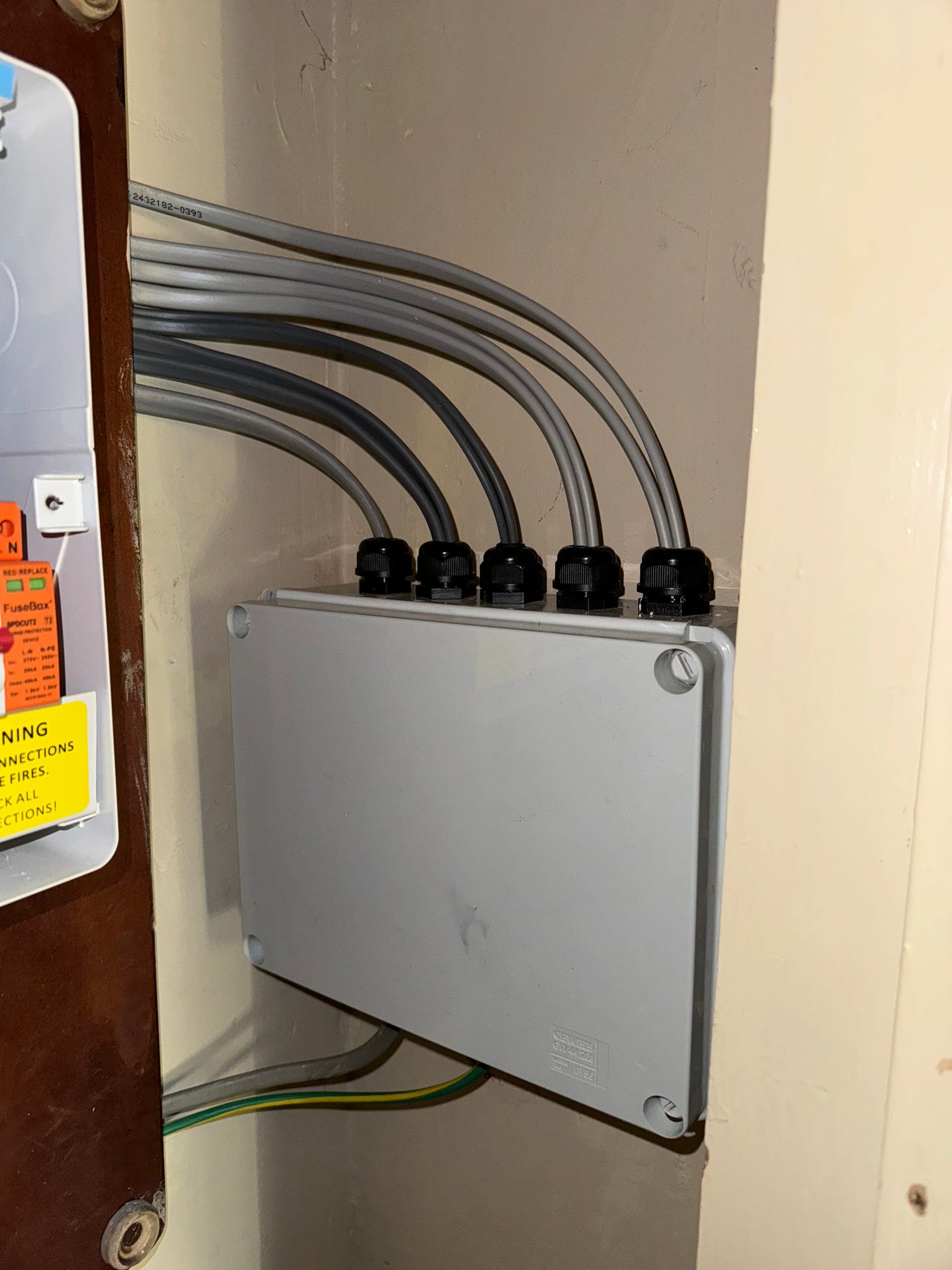 Weatherproof junction box with five glanded cables running into it, mounted beside the consumer unit
