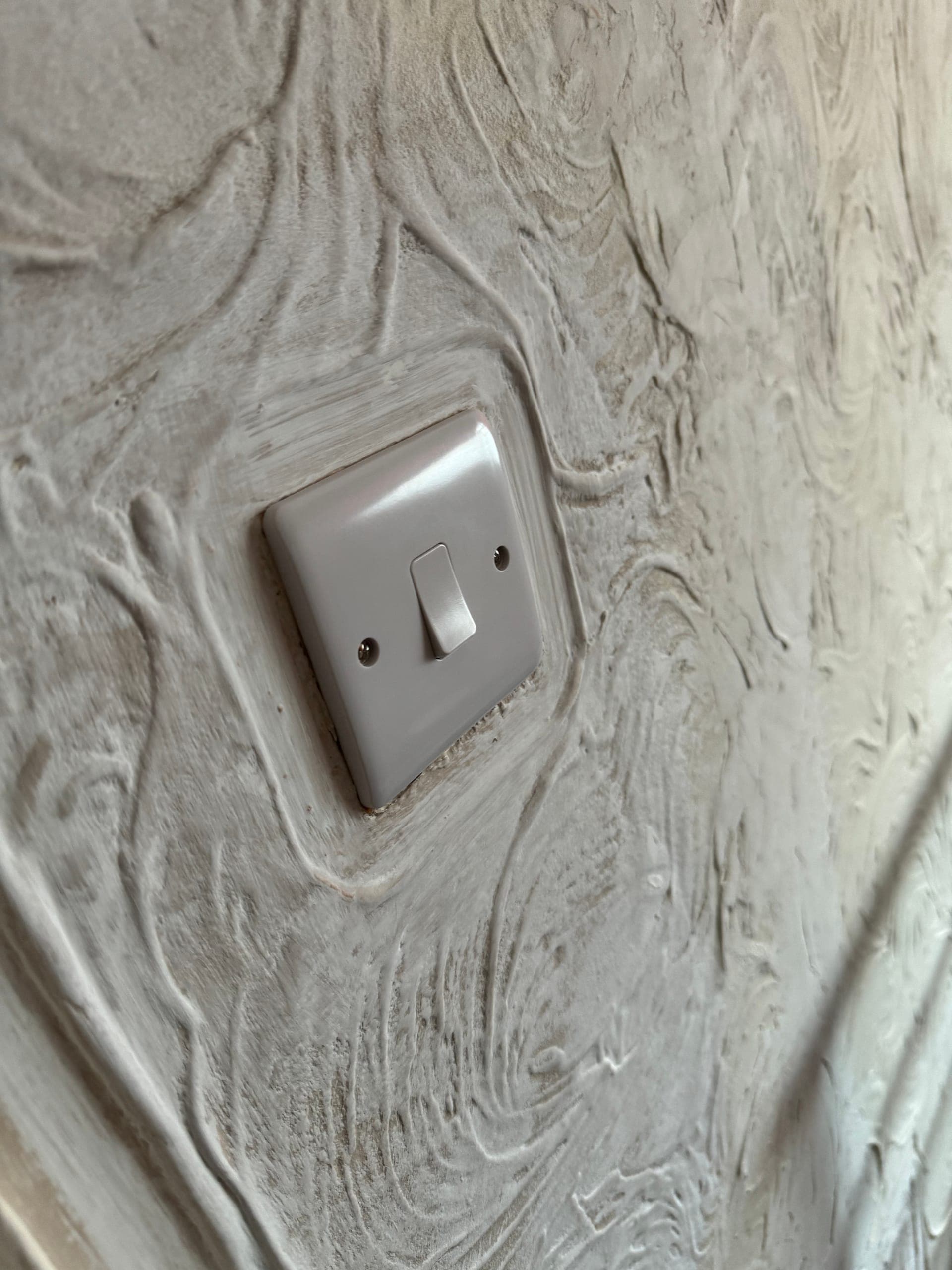 Single light switch fitted to a freshly plastered textured wall