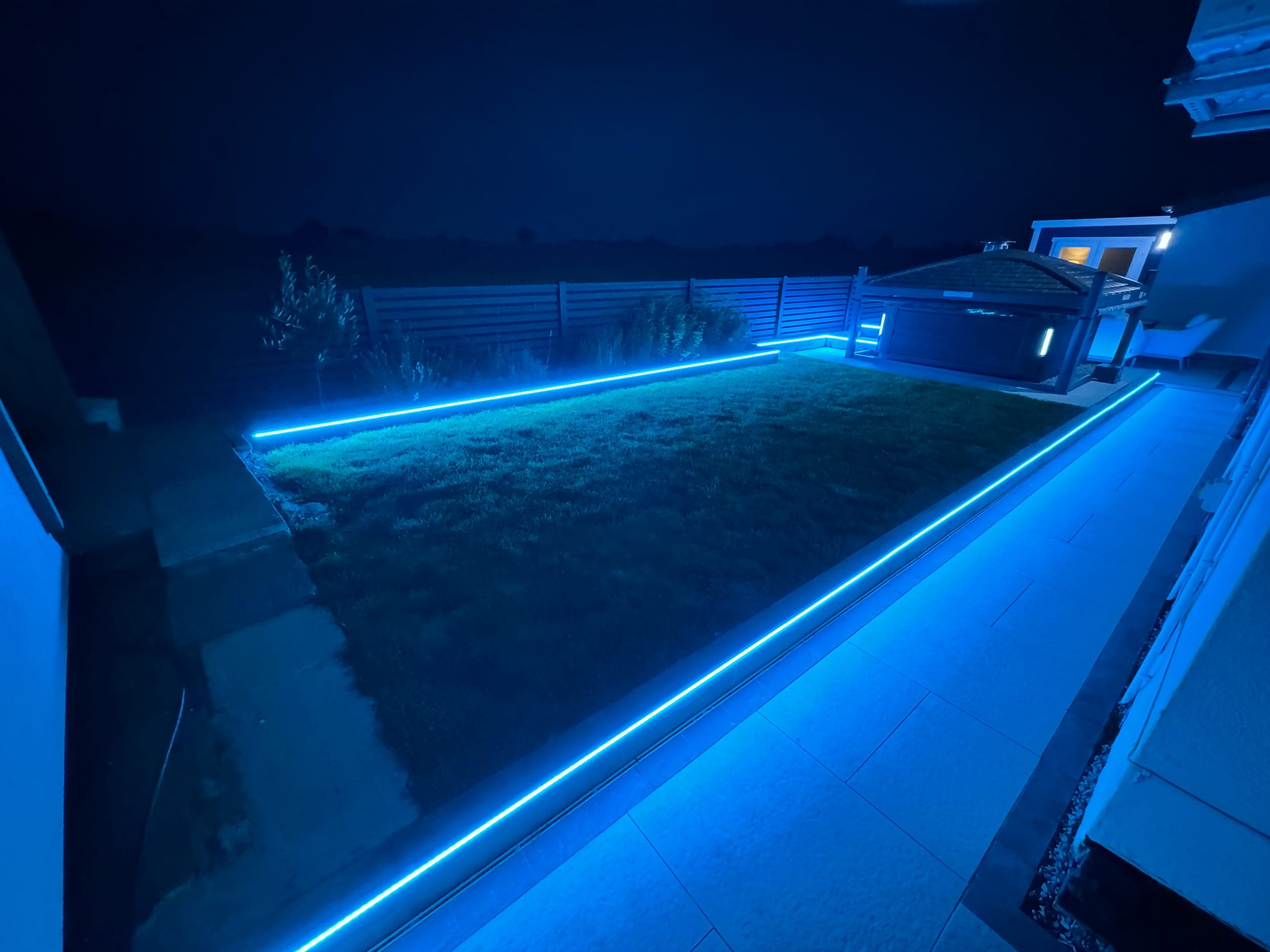 The same garden lighting installation set to blue, tracing the lawn edge and patio
