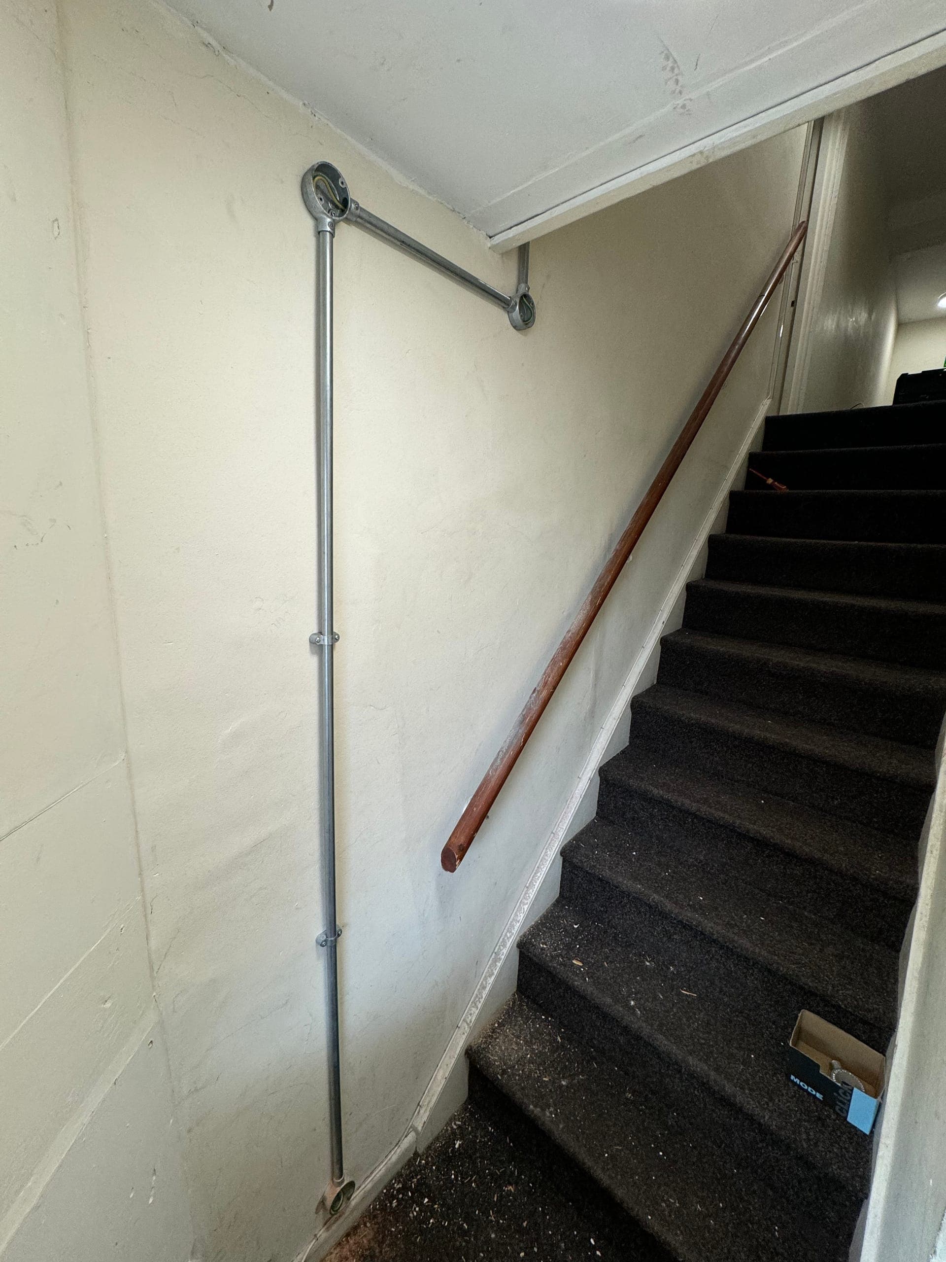 Galvanised steel conduit run down a stairwell wall to a circular junction box at ceiling level