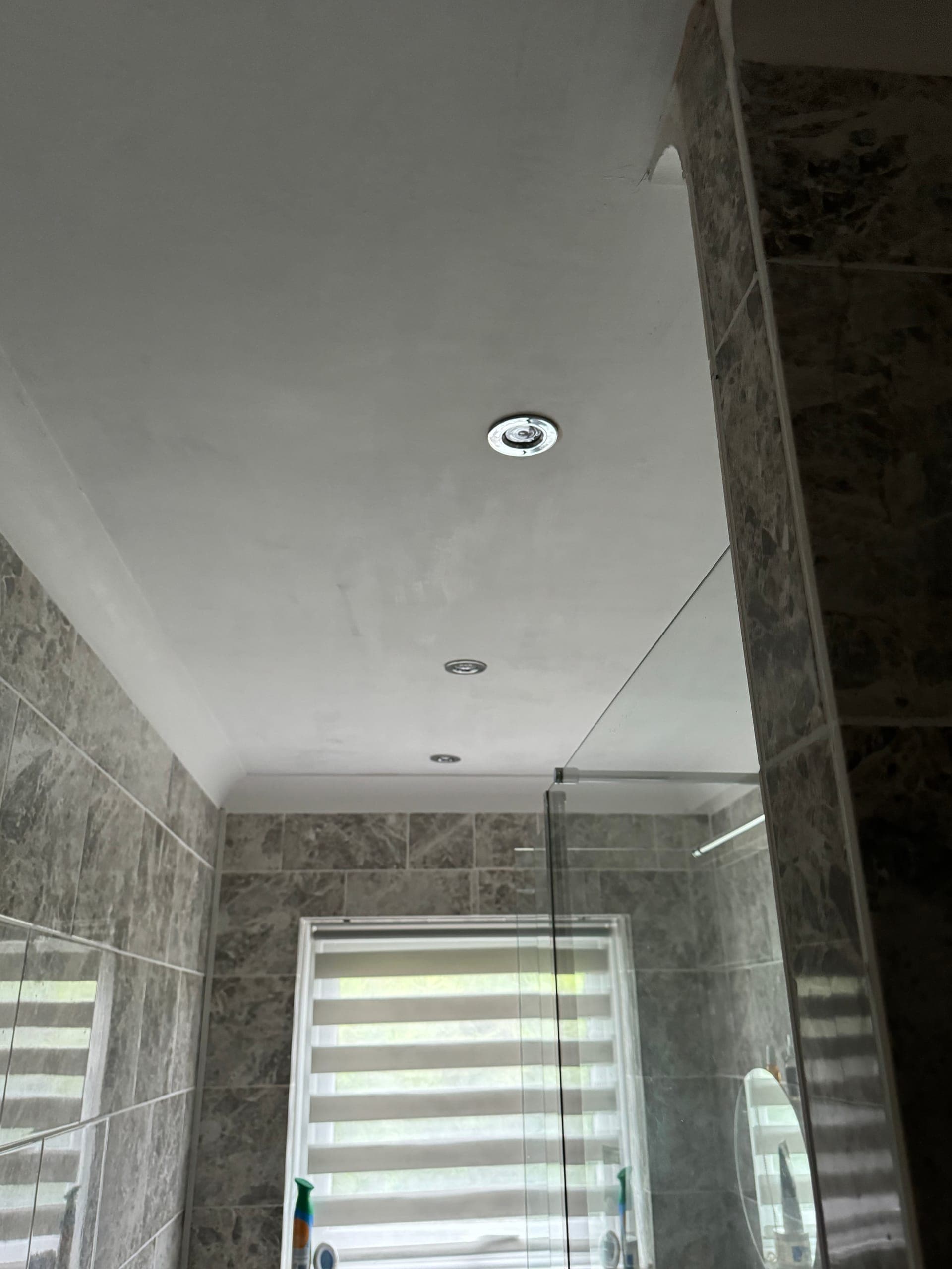 Bathroom ceiling with recessed downlights and an extractor fan above a tiled shower enclosure